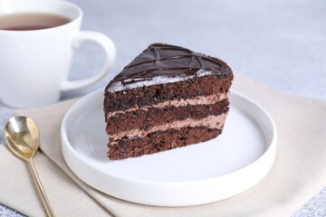 Piece of delicious chocolate cake and spoon on grey table, closeup