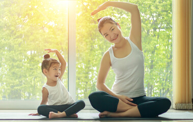 Asian mom practice yoga at home with a adorable daughter sitting next to her while exercise at home in the morning