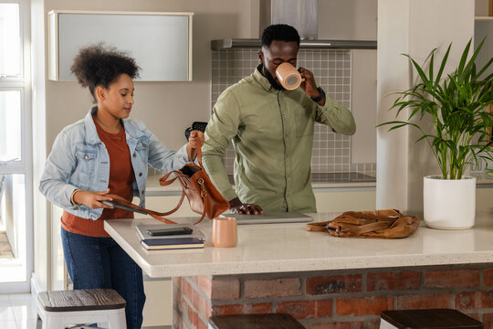 Couple preparing for day, woman packing bag, man drinking coffee in kitchen