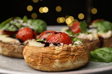Tasty stuffed mushrooms served on black table against blurred background, closeup. Bokeh effect
