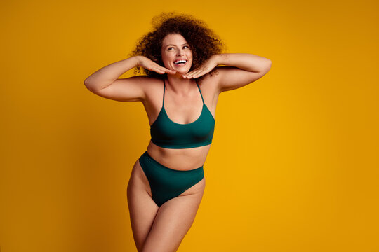 Confident curly haired woman in green lingerie posing against a bright yellow background