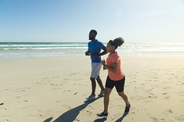 Fototapeta premium African American couple jogging on beach, enjoying sunny day and ocean view