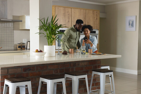 Couple in kitchen smiling and looking at smartphone, enjoying quality time together