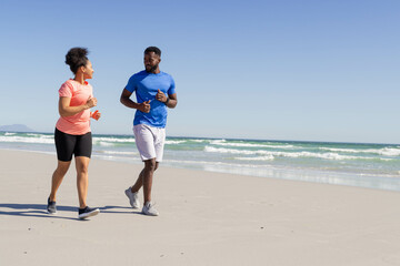 Fototapeta premium Couple jogging on beach, enjoying sunny day and staying active together, copy space