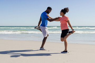 Fototapeta premium African American couple stretching together on beach, enjoying sunny day by ocean