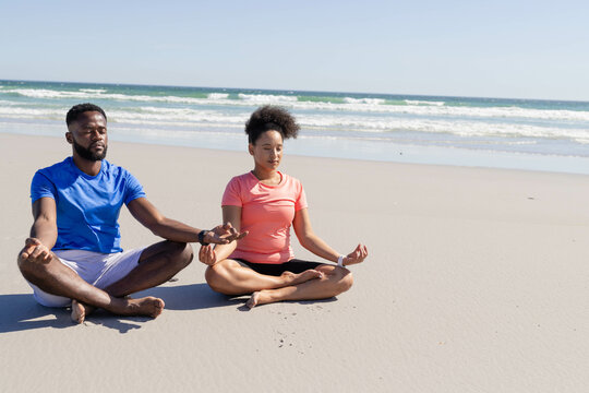 Couple meditating on beach, practicing mindfulness and relaxation by ocean waves