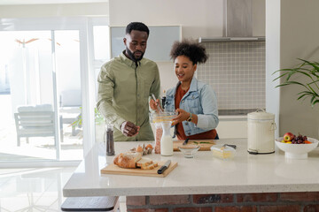 Couple in kitchen preparing meal together, mixing ingredients and smiling warmly