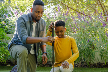 Father and son bonding while practicing golf together in sunny backyard