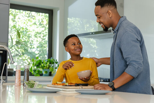 African American father and son enjoying breakfast together in modern kitchen, sharing smiles