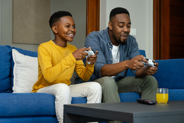 African American father and son playing video games on couch, enjoying quality time together