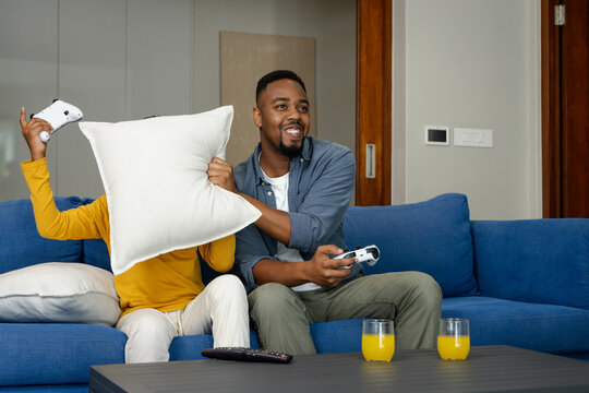 African American father and son playing video games in living room with controllers, orange juice