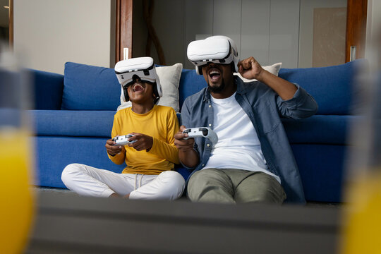 African American father and son using VR headsets and gaming controllers, enjoying virtual reality