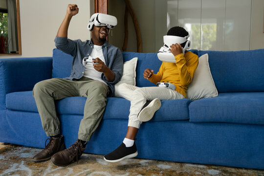 African American African American father and son playing video games with VR headsets on sofa
