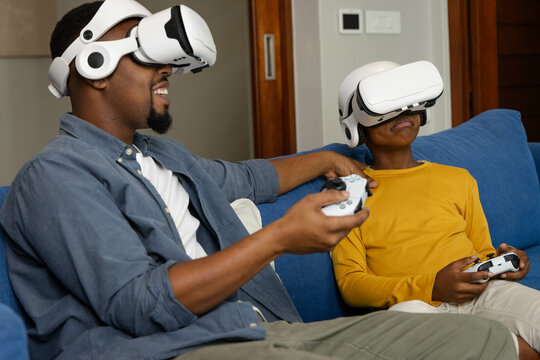 African American father and son enjoying virtual reality gaming together on living room couch