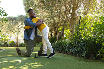 African American father hugging young boy on green lawn with golf ball and putter