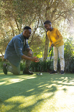 African American father teaching son to play golf on sunny day outdoors