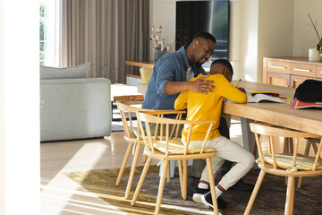 African American father and boy helping study at modern dining area, reviewing books and materials