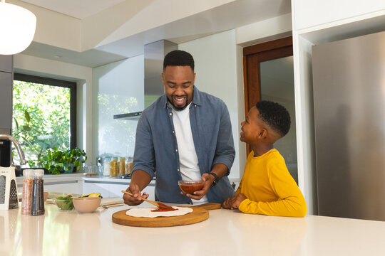 Father and son making homemade pizza together in modern kitchen, enjoying time
