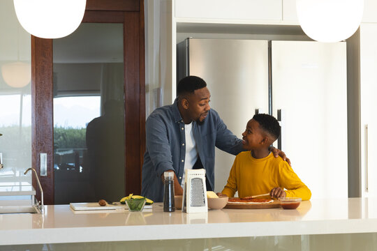 Preparing meal together in modern kitchen, African American father and son smiling
