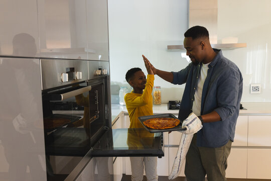 Father and son celebrating successful pizza baking in modern kitchen