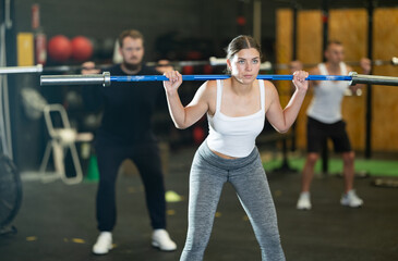 Sportive young woman training with gym rod in sports hall during crossfit workout