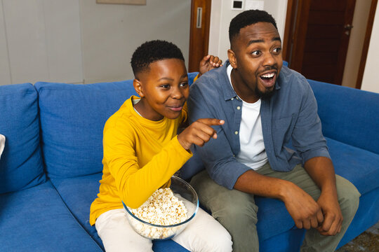 Father and son enjoying movie night on couch with popcorn, feeling excited