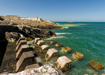 Scenic coastal view with rocky shoreline and concrete sea defenses vibrant turquoise waters under clear skies.