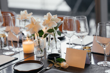 Elegant table setting for a sophisticated celebration on a luxurious black table. Golden candleholders, wine glasses, white rose, napkins, and a paper name card create a refined atmosphere.