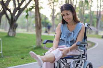 Obraz premium A smiling elderly woman in a wheelchair sits outdoors with her caregiver, sharing a hopeful conversation during a rehabilitation treatment for arthritis in her leg.