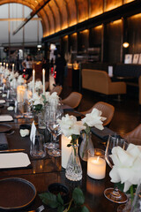 Elegant table setting for a sophisticated celebration on a luxurious black table. Golden candleholders, wine glasses, white rose, napkins, and a paper name card create a refined atmosphere.