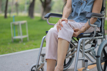 A smiling elderly woman in a wheelchair sits outdoors with her caregiver, sharing a hopeful conversation during a rehabilitation treatment for arthritis in her leg.