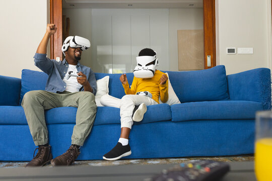 African American father and son playing video games with VR headsets on couch