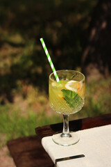 Drink on a garden table on a hot summer day. Glass with cocktail on a wooden table outdoors. Lemonade on a table against the background of blurred nature. Lemonade or other drink in a glass goblet