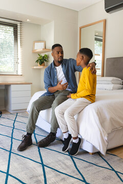 African American father helping young boy get ready for bed in bedroom with dresser and plant