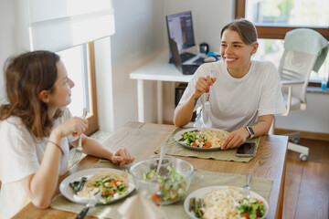 Two good friends are happily enjoying a delicious and healthy meal together in a cozy, modern dining space