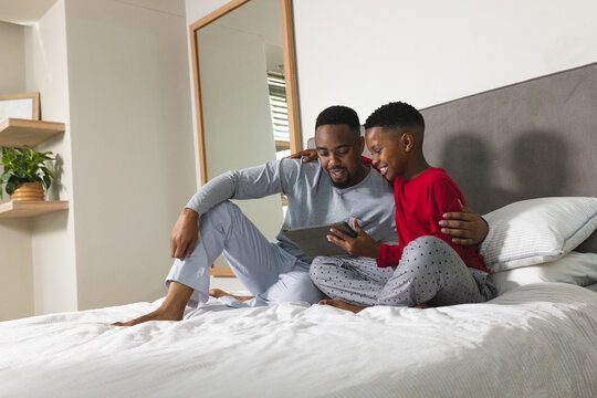 Father and son sitting on bed using tablet, enjoying quality time together