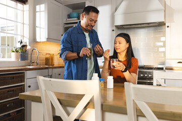 Asian couple in kitchen taking vitamins together, enjoying healthy lifestyle