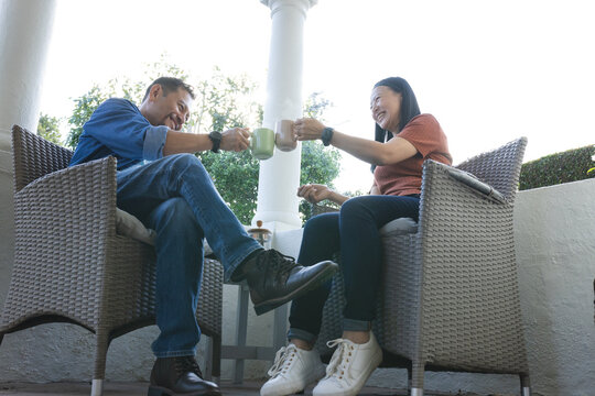Mature Asian couple enjoying coffee together on patio, smiling and relaxing outdoors - Powered by Adobe