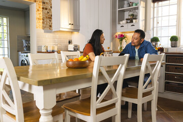 Asian couple enjoying conversation at kitchen table with fruit bowl centerpiece