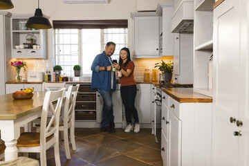 Mature Asian couple in kitchen looking at smartphone, enjoying morning together