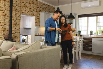 Mature Asian couple using tablet in cozy kitchen, planning home renovation together