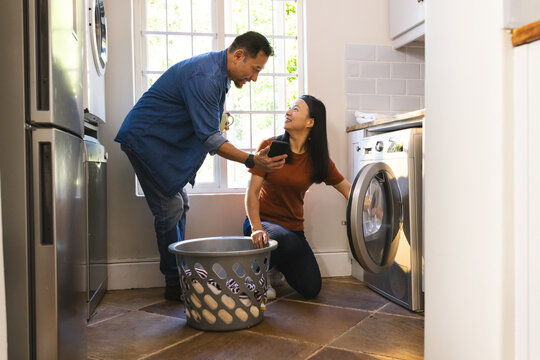 Mature Asian couple doing laundry together at home, sharing lighthearted moment