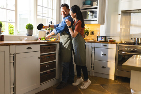 Mature Asian couple cooking together in kitchen, smiling and enjoying quality time