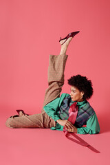 Young woman showcases vibrant fashion style while posing creatively on a pink background