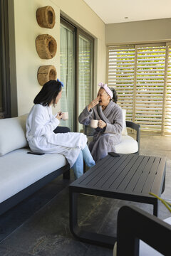 Asian mother and daughter chatting on outdoor patio with coffee cups and black coffee table