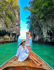 On a sunny day, a traveler enjoys a peaceful experience aboard a wooden longtail boat. Verdant cliffs and clear turquoise waters of Koh Hong Island create a breathtaking backdrop for relaxation.