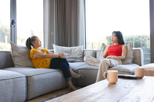 Asian senior mother and daughter having heartfelt conversation on living room sofa