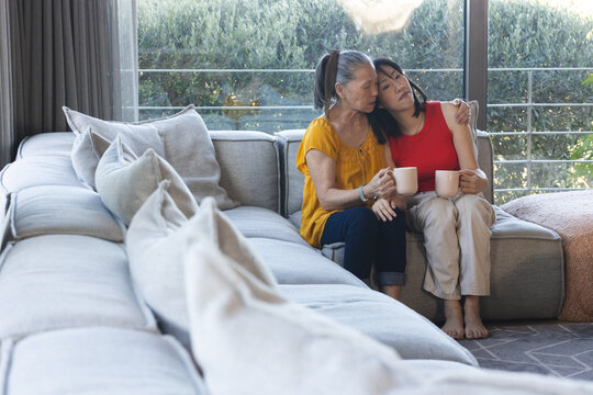 Elderly woman comforting young woman on couch, both holding coffee mugs