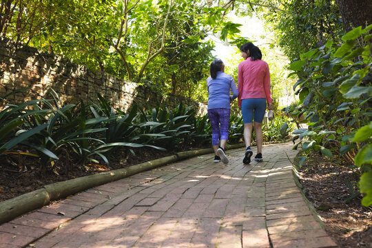 Asian senior mother and daughter walking on garden pathway, enjoying bright vibe with lush greenery