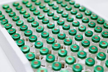 A large number of ampoules with green caps arranged in a box on a white background. Concept organization and storage of medical substances in a sterile laboratory environment.